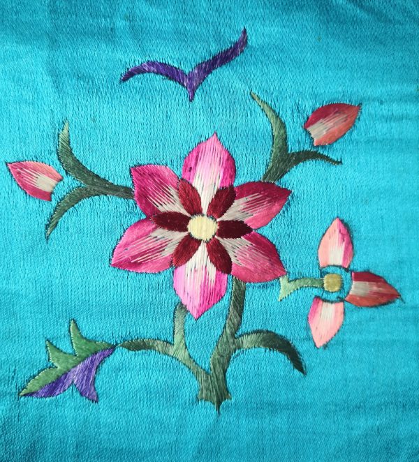 Pink and cream embroidered flowers and green leaves on turquoise fabric