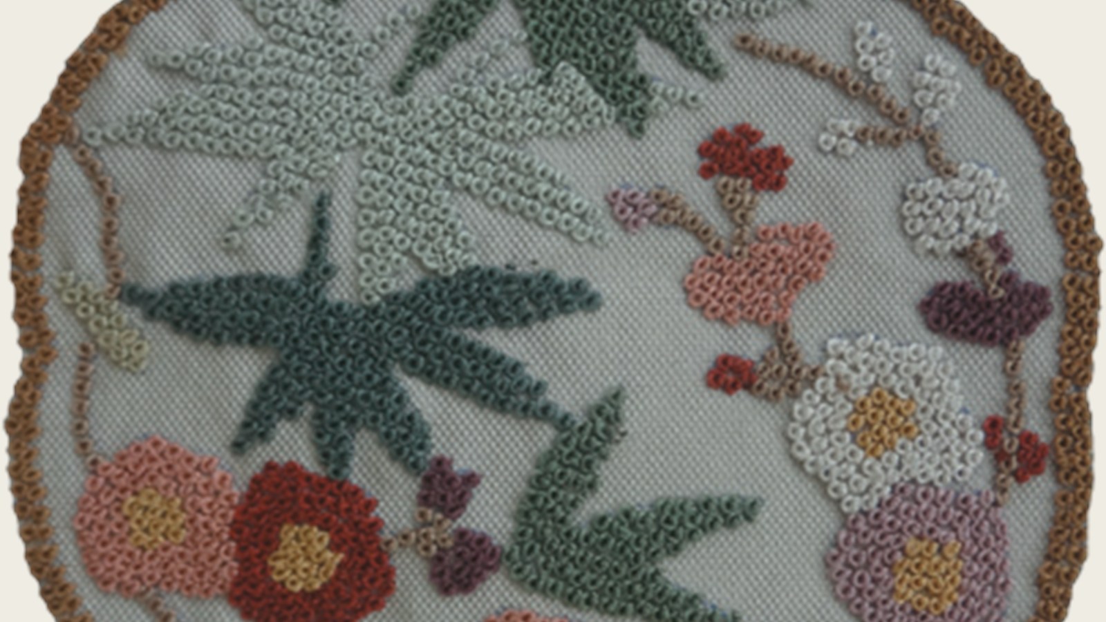 Close-up of dense dazi embroidery forming bamboo leaves and flowers on a round embroidered panel.