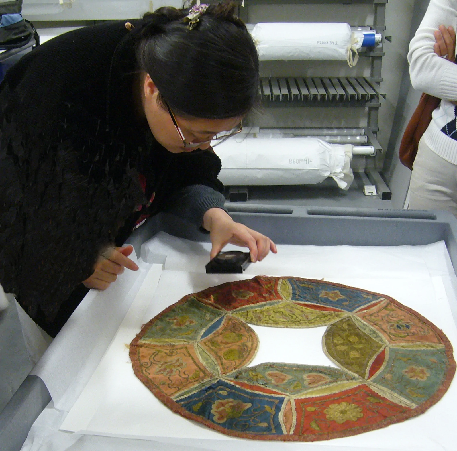Shao Xiaocheng examining and assessing an embroidered textile at the Asian Art Museum in San Francisco
