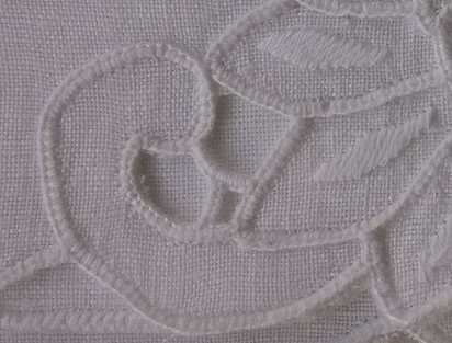 Detail of the white chrysanthemum napkin, showing a curled stitched contour, open spaces and the visible weave of retained cloth.