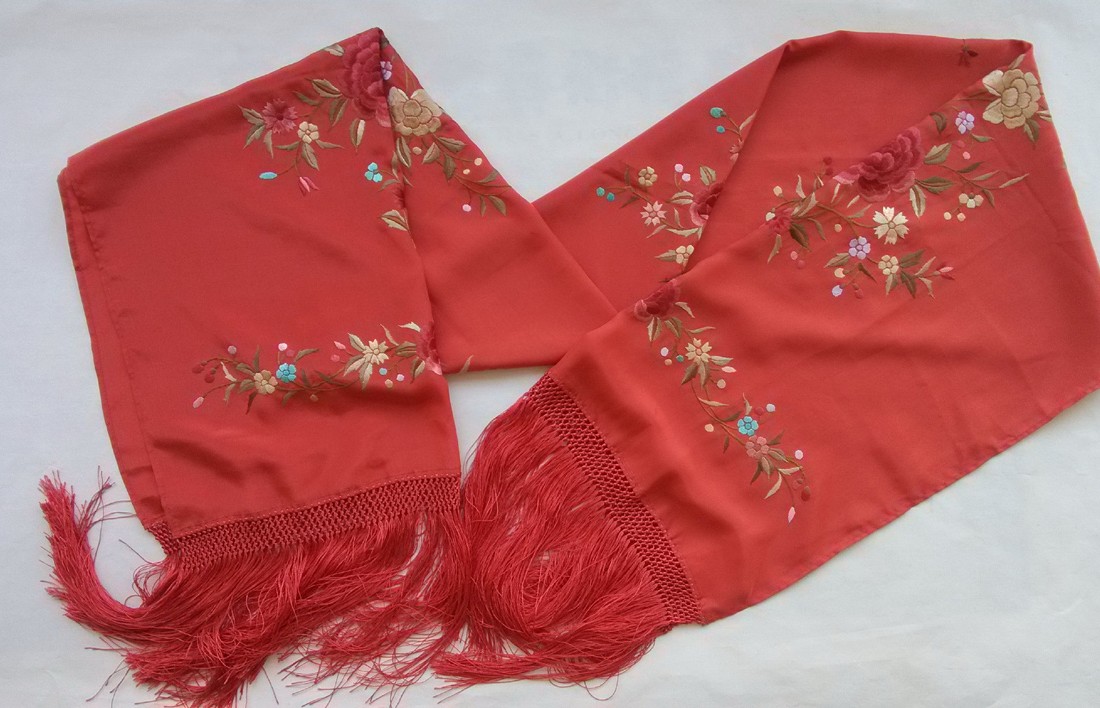 Red embroidered silk scarf folded into overlapping lengths, with multicoloured flower groups, visible red ground and matching red fringed ends.