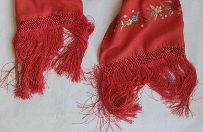 Original close view of two red scarf ends, showing matching loose fringe below narrow open bands and a small embroidered flower passage above one end.
