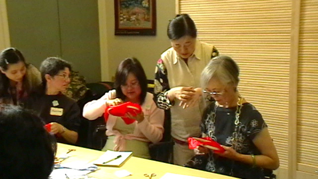 Participants handling red fabric and embroidery materials around a table in a 2008 San Francisco archive photograph.
