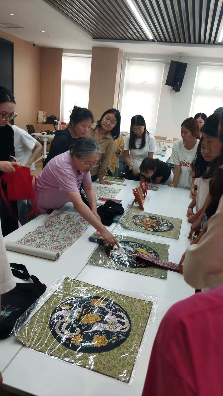 A group gathered around embroidery works laid out on a table.
